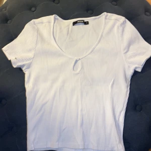 Vit ribbad topp från Bik Bok - Säljer en vit ribbad topp från Bik Bok i storlek M. Toppen har en v-ringad design med korta ärmar och en liten knapplösning framtill. Perfekt för en sommar dag