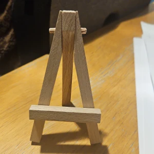 Litet trästaffli - Säljer ett litet och smidigt trästaffli, perfekt för att visa upp små konstverk eller foton. Staffliet är tillverkat av ljust trä och har en enkel, klassisk design. Det är hopfällbart för enkel förvaring och transport. Frakt ingår ej.