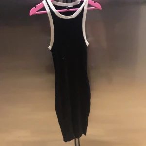 Svart ribbad klänning från H&M - Snygg svart ribbad klänning från H&M med vita kanter. Perfekt för en stilren look. Klänningen är ärmlös och har en väldigt Stretch passform.