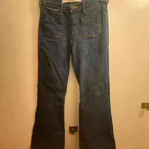 Blå bootcut jeans Wrangler - Säljer ett par klassiska mörkblå/denim bootcut jeans från Wrangler. Snygg passform med mid/highrise. Fina detaljer. Är 163cm lång och byxorna går ner i golvet, har därför vikt upp dem vilket resulterat i lite slitage (som knappt syns, ljusare streck där byxorna varit vikta). Riktigt coola 70-tals jeans! ⭐️⭐️💞