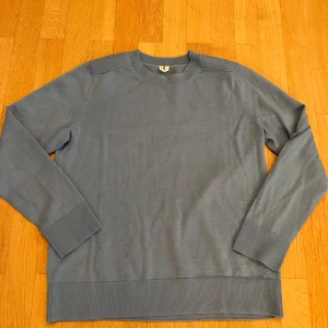 Blå ulltröja från A Day's March - Säljer en stilren blå tröja från A Day's March i 100% ull. Tröjan har en klassisk design med långa ärmar och ribbade muddar vid ärmslut och nederkant. Perfekt för kyligare dagar.