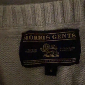 Grå stickad tröja från Morris Gents - Säljer en stilren grå stickad tröja från Morris Gents med tryck på framsidan. Tröjan har en rund halsringning och långa ärmar, perfekt för kyligare dagar. Passar bra till både jeans och chinos.