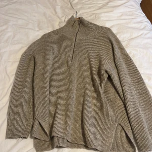 Beige ribbad tröja från Gina Tricot - Säljer en stilren beige ribbad tröja från Gina Tricot med dragkedja i halsen. Perfekt för kyligare dagar med sin höga krage och långa ärmar. Tröjan har en avslappnad passform och är gjord i ett mjukt material.