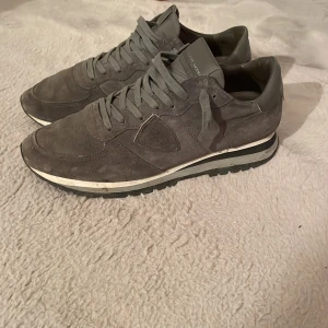 Grå sneakers från Philippe Model - Snygga grå sneakers från Philippe Model i mocka med snörning. Perfekta för en stilren look med en bekväm passform. Diskret design med en vit sula som ger en modern touch.