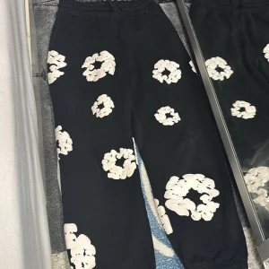 Svarta byxor med blommönster från Denim Tears - Snygga svarta byxor från Denim Tears med ett unikt vitt blommönster. Byxorna har en loose passform och elastisk midja för extra komfort. Perfekta för en avslappnad stil.