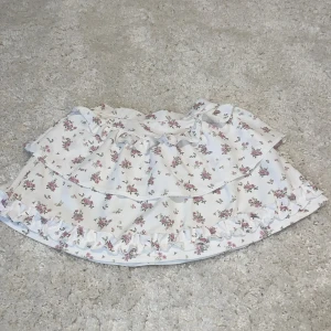 Blommig volangkjol - Charmig kortkjol med blommigt mönster och volangdetaljer. Perfekt för en somrig look med sin lätta och luftiga design.