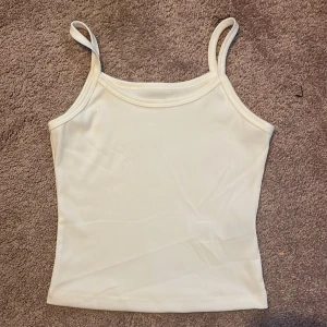 Vit ribbad linnetopp (OBS) oanvänd! - Säljer en stilren vit ribbad linnetopp med smala axelband. Perfekt för varma sommardagar eller som ett basplagg i garderoben.