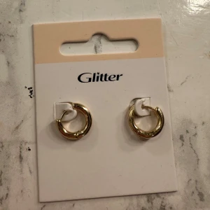 Guldiga örhängen från Glitter - Snygga guldiga örhängen från Glitter. Ena örhänget har en glittrig detalj med små stenar, De är runda och enkla. Den är helt nya men säljer de det inte riktigt var min stil. Båda två för priset, men om du skulle vilja ha ett par är det bara att skriva till mig.