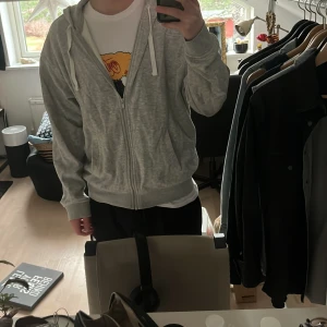 Grå huvtröja från H&M - Säljer en grå huvtröja från H&M i relaxed fit. Tröjan har dragkedja och en praktisk huva med vita snören. Perfekt för en avslappnad stil.