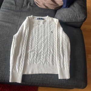 Vit stickad tröja från Polo Ralph Lauren - Vit stickad tröja från Polo Ralph Lauren med kabelstickat mönster och den klassiska loggan på bröstet. 