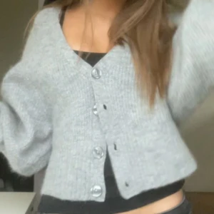 Grå ribbad kofta från Gina Tricot - Säljer en mysig grå kofta från Gina Tricot i premiumkvalitet. Koftan är ribbad med knappar framtill och har en croppad passform. Perfekt för kyligare dagar! Priset kan diskuteras! Inte använd många gånger🥰