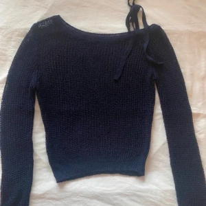 Mörkblå stickad tröja med knytband - Säljer en mörkblå stickad tröja med långa ärmar och ett dekorativt knytband vid halsen. Perfekt nu till vinter och verkligen snygg till det mesta🫶i mycket bra skick då den tyvärr knappt har kommit till användning!💘