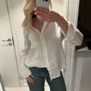 Vit linneskjorta - Säljer en stilren vit skjorta i 100% linne. Skjortan har en klassisk design med knappar framtill och långa ärmar. Perfekt för en avslappnad men ändå elegant look.