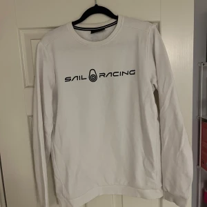 Vit tröja från Sail Racing - Vit långärmad tröja från Sail Racing med svart text på bröstet. Storlek 170 vilket motsvarar small. 