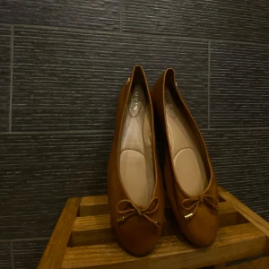 Bruna ballerinaskor från Ralph Lauren - Bruna ballerinaskor från Ralph Lauren med en söt rosett framtill. Materialet är i skinn med RLL logga längst sidan. Säljer dessa fina skor då de är lite för små för mig. Orginalpris (1480kr) 