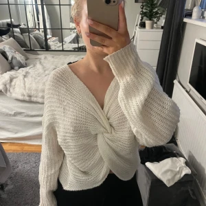 Vit stickad tröja med knutdetalj - Säljer en mysig vit stickad tröja med en unik knutdetalj framtill. Tröjan har långa ärmar och en lös passform, perfekt för kyligare dagar. Den är både stilren och bekväm, ett måste i garderoben!