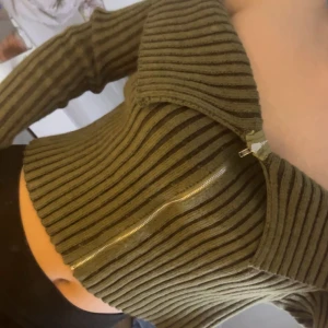 Olivgrön ribbad tröja med dragkedja - Snygg olivgrön ribbad tröja med dragkedja framtill. Tröjan har långa ärmar och en croppad passform som ger en trendig look. Perfekt för att hålla stilen i höst och vinter. Den är lite oversized