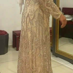 Champagnefärgad glittrig långklänning/festklänning - Elegant champagnefärgad långklänning med glittriga detaljer. Klänningen har långa ärmar och ett vackert mönster av paljetter som ger en lyxig känsla. Perfekt för festliga tillfällen. Klänningen är helt ny aldrig använt säljs för 2500kr
