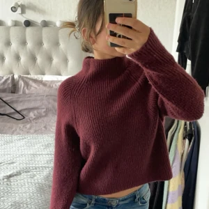 Vinröd stickad tröja - Säljer en mysig vinröd stickad tröja med hög krage. Tröjan är croppad och har långa ärmar, perfekt för kyliga dagar. Passar bra till jeans eller kjol för en avslappnad look.