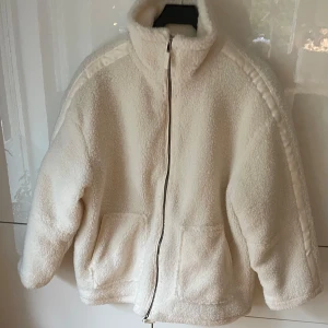 Vit teddyjacka med dragkedja - Mysig vit teddyjacka med dragkedja framtill. Jackan har en quiltad insida och två praktiska fickor. Perfekt för kyliga dagar när du vill hålla dig varm och bekväm.✨