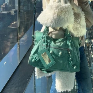 Grön/ blå balenciaga väska - Snygg grön /blå  med unika detaljer som en liten spegel och dragkedja. Väskan har flätade handtag och dekorativa nitar. Jätte jätte fin balenciaga väska och jätte fin färg!!! Modell city bag!!
