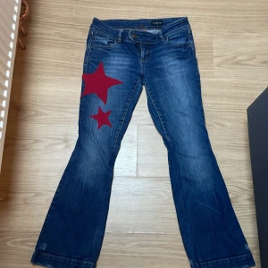 Blå jeans med röda stjärnor - Snygga blå jeans  unika röda stjärnor på ena benet. De har en klassisk femficksdesign och en knappgylf. De är lowwasited och bootcot