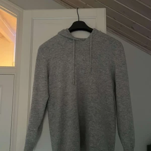 Grå merinoull hoodie - Säljer en stilren grå merinoull hoodie i fint skick och justerbar huva. Perfekt för en avslappnad look. Tröjan är bara använd cirka 5 gånger så är väldigt bra skick. Hör av er för om ni undrar minsta lilla 