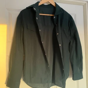Mörkgrön skjorta i polyester - Snygg mörkgrön skjorta i 100% polyester med knappar framtill. Perfekt för en stilren look. Skjortan har långa ärmar och en klassisk krage. Köpt från Shein och endast provad. 
