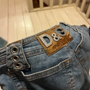 Blå jeans från D&G - Snygga blå jeans från D&G med Midwaisted bootcut-stil. De har knappar framtill och detaljer vid midjan. 