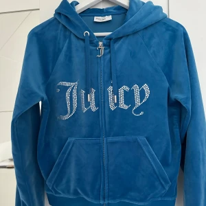 Blå velourjacka från Juicy Couture!🩵 - Snygg blå velourjacka från Juicy Couture med glittrande stenar som bildar texten 'Juicy' på framsidan. Jackan har en dragkedja med ett dekorativt 'J'-hänge och en mysig huva med knytband!😻Säljer den för att den inte används! Hör av er på dm via intresse!❤️