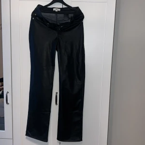 Svarta skinnbyxor - Snygga svarta skinnbyxor med hög midja och raka ben. Byxorna har dragkedja och knappar framtill samt fickor både fram och bak. Perfekta för en stilren look.
