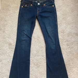 True Religion Joey Low Rise Flare Jeans - Snygga True Religion Joey jeans med låg midja och flare stil. Mörkblå denim med kontrastsömmar och klassiska bakfickor med lock och knapp. Perfekta för en trendig look. Jag kollar efter någon som vill byta storlek jag har 24 på dom här men skulle vilja BYTAS til 23 dom är i nyskick och få tal använda hör av dig om du undrar något 💗