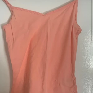 Persikofärgad linnetopp i ekologisk bomull - Säljer en persikofärgad linnetopp från märket Cubus, tillverkad i ekologisk bomull. Toppen har smala axelband och en enkel design som passar perfekt för varma dagar. Perfekt för dig som vill ha något bekvämt och stilrent. 