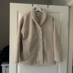 Beige teddyjacka  - Mysig beige/ creamvit teddyjacka från Carin Wester med långa ärmar och en avslappnad oversized passform. Perfekt för kyliga dagar när du vill hålla dig varm och stilren. Jackan har en enkel design utan synliga detaljer som dragkedjor eller knappar.