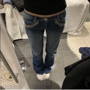Blå jeans med broderade detaljer - Snygga blå jeans med unika broderade detaljer på fickorna. De har en låg midja och en bootcut-stil som ger en avslappnad look. Perfekta för dig som vill ha något annorlunda i garderoben. Midjemått 37 och innerbenslängd 78, använd gärna köp nu 💗