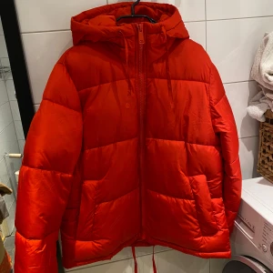 Röd pufferjacka från H&M - Säljer en snygg röd pufferjacka från H&M. Jackan har en dragkedja framtill och en mysig huva. Perfekt för kyliga dagar med sin vadderade design. Storlek XS men passar upp till L.