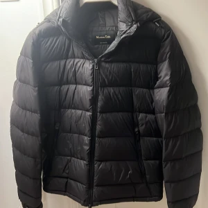 Svart pufferjacka från Massimo Dutti - Snygg svart pufferjacka från Massimo Dutti med dragkedja och huva. Perfekt för kyliga dagar med sin quiltade design. Jackan har långa ärmar och två fickor med dragkedja framtill. Storlek S. Pris kan diskuteras vid snabbaffär!