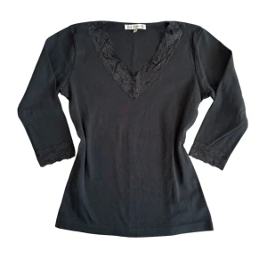Svart topp med spetsdetaljer - Snygg svart topp med v-ringning och spetsdetaljer vid hals och ärmslut. Toppen har trekvartsärmar och en elegant passform. Perfekt för en stilren look.