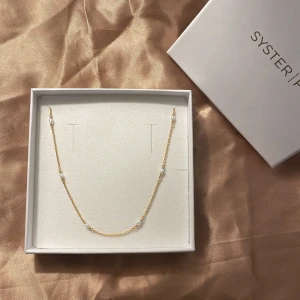 Guldhalsband med pärlor från Syster P - Elegant guldhalsband från Syster P med små vita pärlor. Perfekt för att ge en touch av lyx till din outfit. Halsbandet kommer i en stilren förpackning.