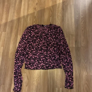 Svart blommig långärmad topp - Snygg svart topp med rosa blommönster. Den har långa ärmar och en bekväm passform. Materialet är genomskinligt. Knappt använd
