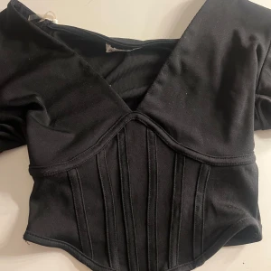 Svart korsettopp - Snygg svart korsettopp med v-ringad design och korta ärmar. Toppen har en ribbad struktur. Väldigt basisk!