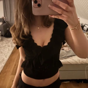 Svart volangtopp - Snygg svart topp med volangdetaljer och djup v-ringning. Perfekt för en stilfull look. Toppen är ärmlös och har en figurnära passform. Tveka inte att höra av dig vid frågor!💞💞💞
