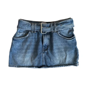 Jeanskjol med bälte - Trendig blå jeanskjol med ett matchande bälte och klassiska fickor fram. Perfekt för en avslappnad stil med en touch av retro. Passar bra till en enkel t-shirt eller en snygg blus.