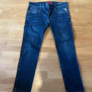 Jeans Replay Anbass W33 L34 - Snygga mörkblå jeans från Replay i modellen Anbass. De har en klassisk femficksdesign med dragkedja och knapp. Jeansen har en normal passform och är perfekta för en avslappnad stil.
