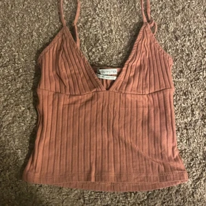 linne från bershka - Säljer en snygg rostfärgad ribbad linnetopp från bershka . Toppen har smala axelband och  v-ringad. Den är typ rosa korall färg 