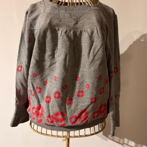 Grå collegetröja med blommönster från ONLY - Säljer en grå collagetröja från ONLY med röda blommor som dekoration. Tröjan har långa ärmar och en bekväm passform. Perfekt för en avslappnad stil med en touch av färg.