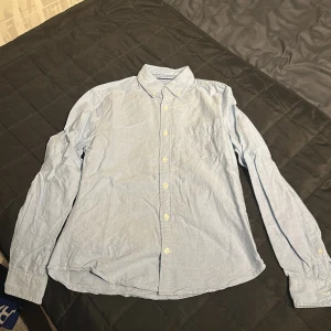 Ljusblå skjorta från Dressmann - Säljer en stilren ljusblå skjorta från Dressmann i slim fit. Skjortan har långa ärmar och klassisk krage med knappar framtill. Perfekt för en snygg och avslappnad look.