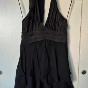 En ny fest klänning  - Elegant svart klänning med djup v-ringning och veckade detaljer. Perfekt för en kväll ute eller en speciell tillställning. Klänningen har en smickrande passform och ett stilrent utseende.