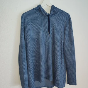 Blå mönstrad hoodie - Säljer en blå hoodie med ett unikt geometriskt mönster. Tröjan har långa ärmar och en justerbar huva med dragsko. Perfekt för en avslappnad stil.