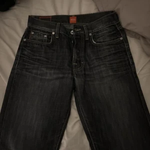 Svarta jeans från Boss - Snygga svarta jeans från Boss med klassisk femficksdesign och subtila slitningar. De har en knappgylf och är perfekta för en stilren look. Passar bra till både vardag och mer uppklädda tillfällen.